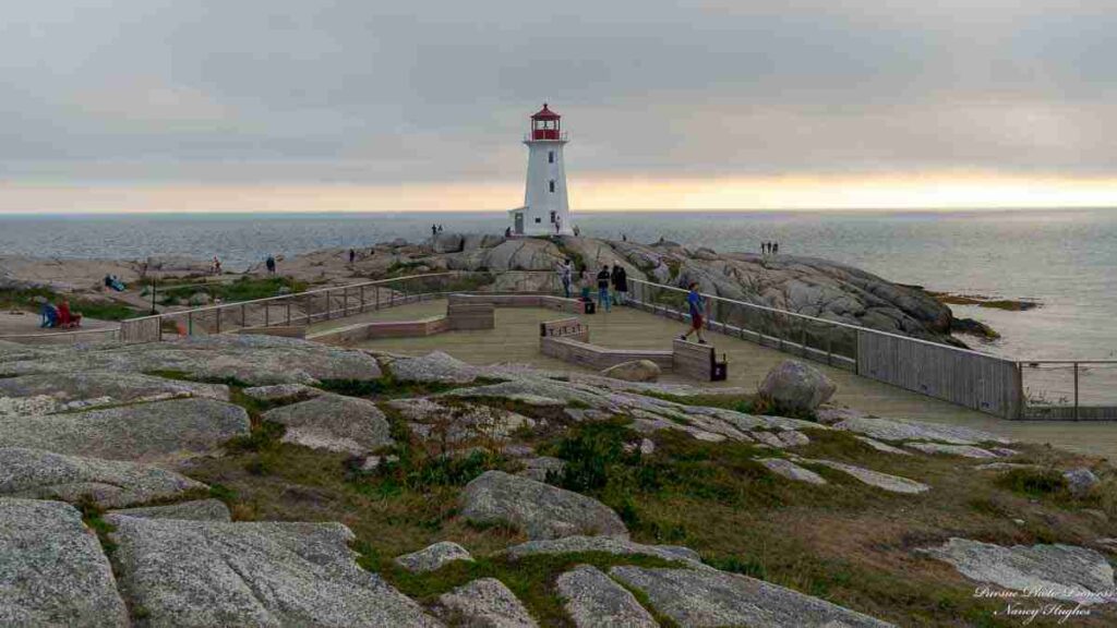 Peggy's Point Lighthouse at Peggy's Cove. Tourists walking around, with a dreary sky in the background.