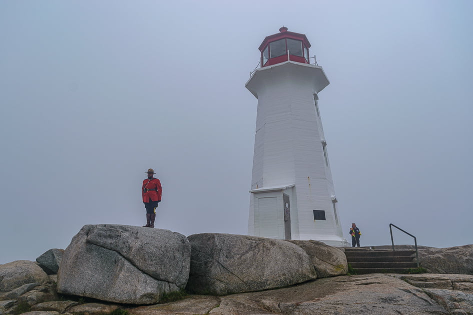 An RCMP Officer standing at attention in front of Peggy's Point Lighthouse in July in the fog