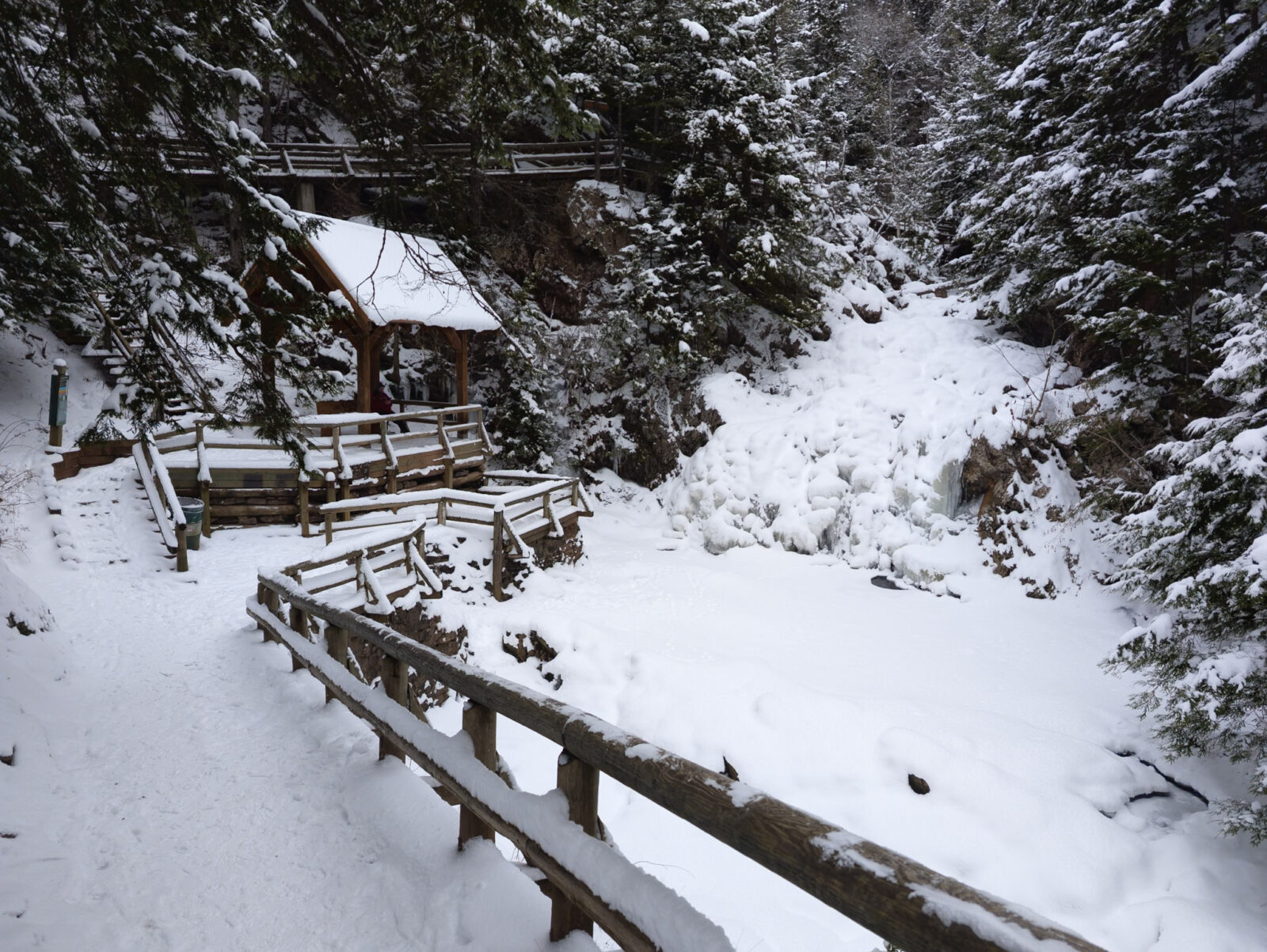 A quiet snow-covered trail and wooden lookout in a forested area of Nova Scotia, creating a peaceful winter scene with frozen waterfall. Victoria Park, Truro.